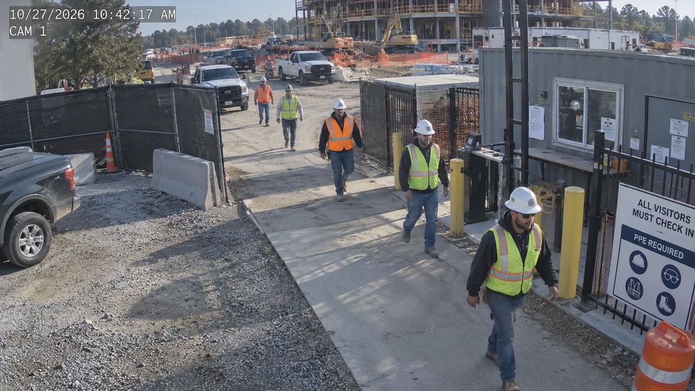 Camera view of workers in full PPE walking through a site checkpoint with a timestamp overlay